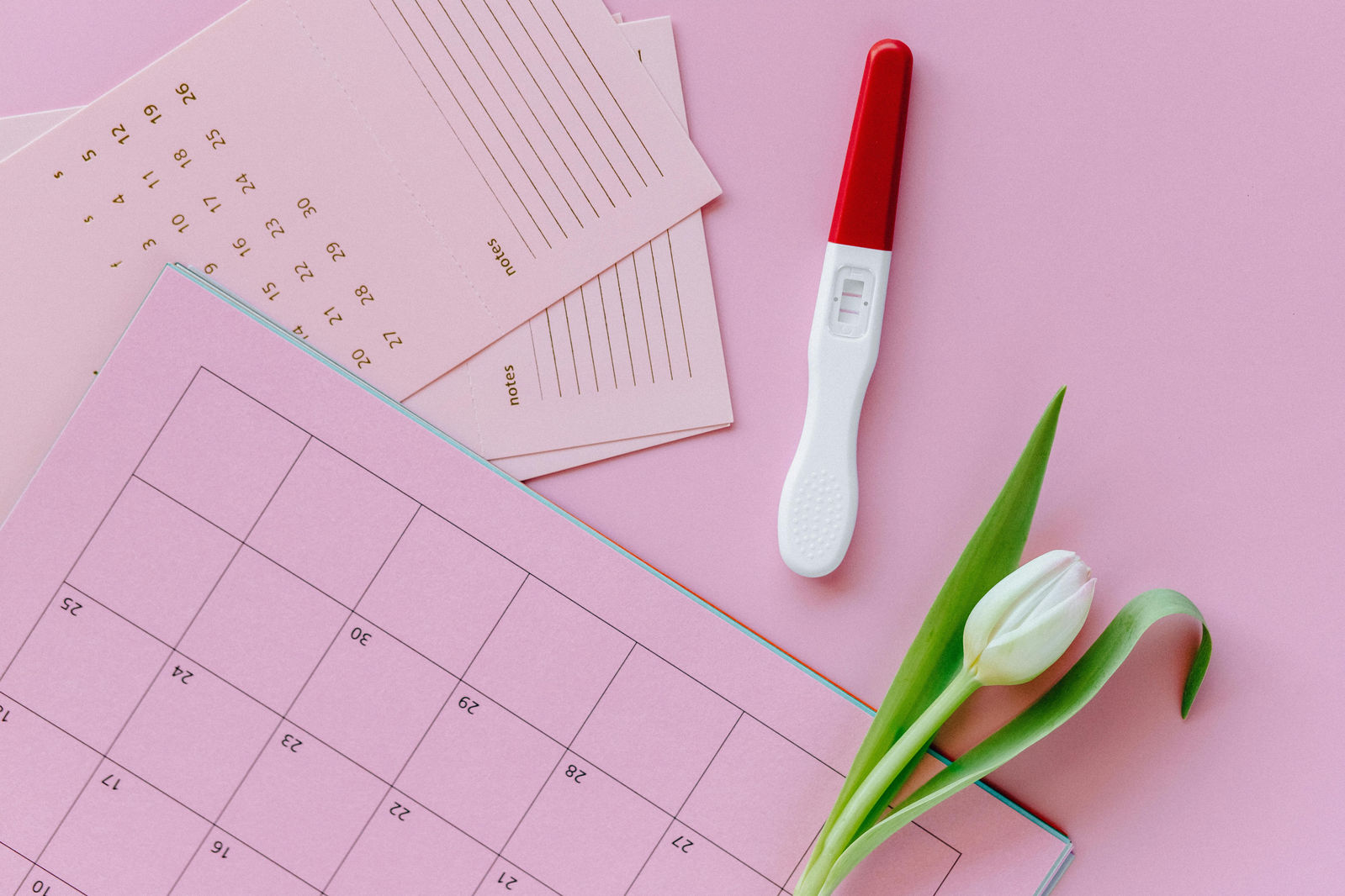 pink period calendar with a positive pregnancy test beside it