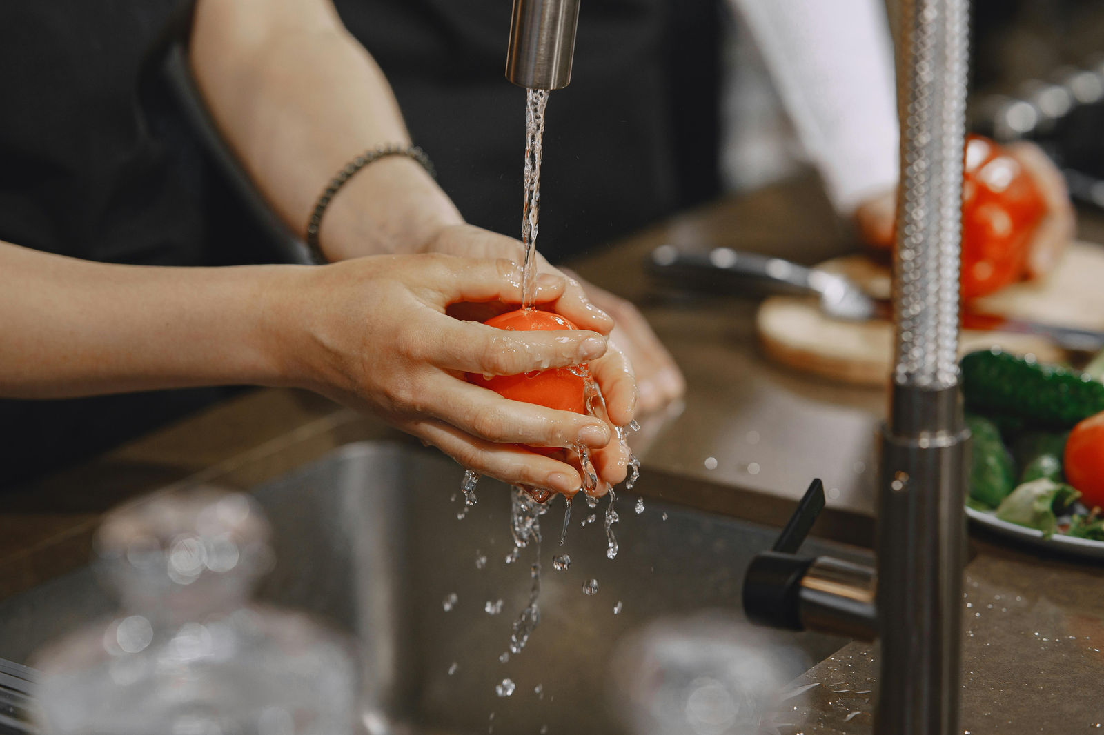 a person washing a tomato in their kitchen sink